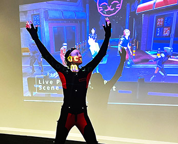 Female in motion capture suit in front of projection screen.