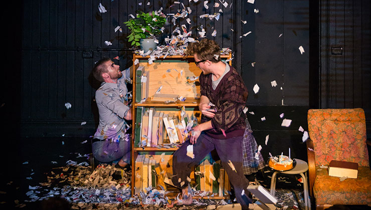 Two men throw torn paper into the air in a stage production